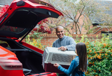 A daughter helps her father load a pet crate into the back of their car.